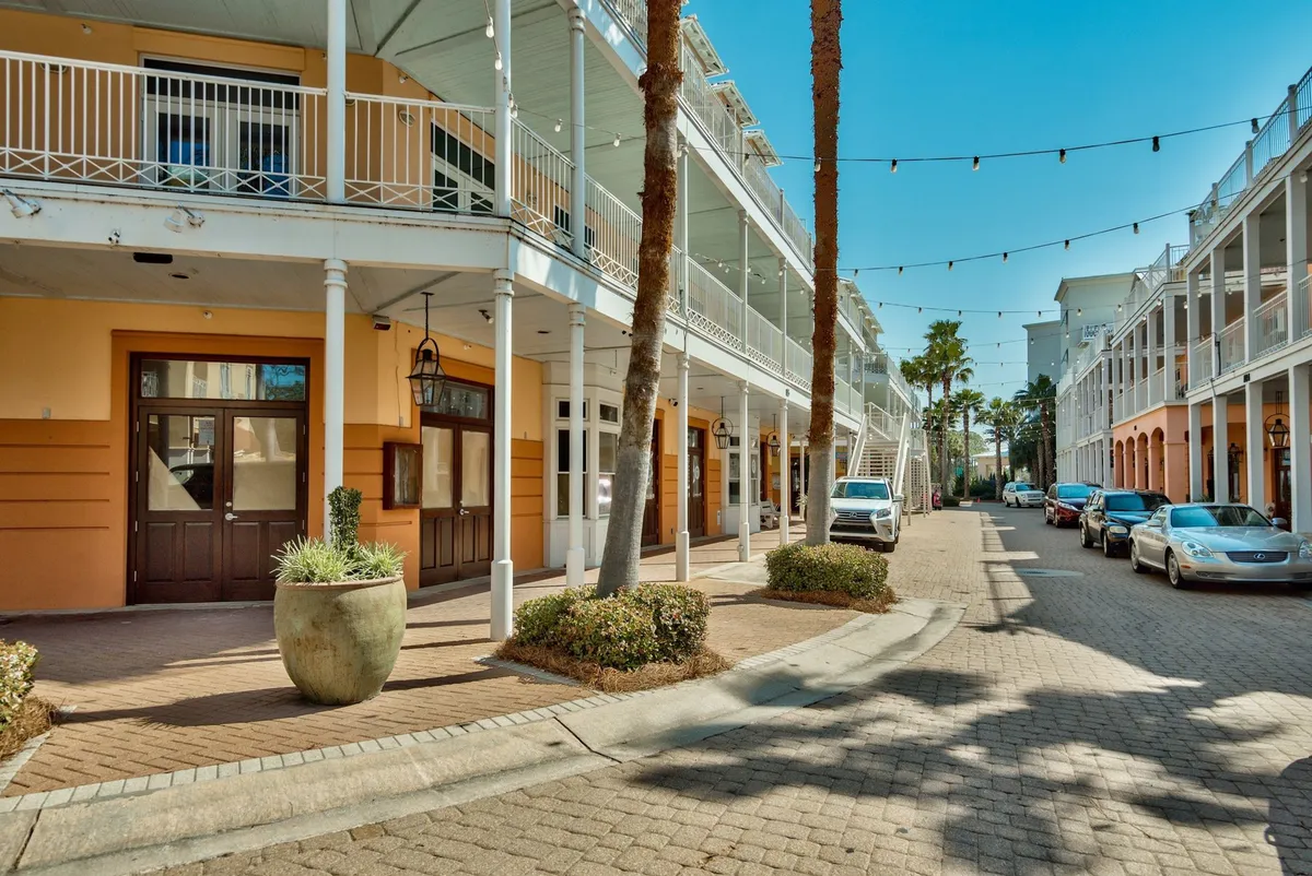 A lively streetscape featuring palm trees, vibrant storefronts, outdoor seating, and hanging string lights, where people enjoy casual dining and strolls, capturing the essence of Carillon’s charming town center.